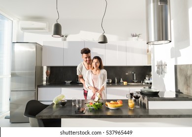 Young Couple Embrace In Kitchen, Hispanic Man And Asian Woman Hug Modern Apartment Interior - Powered by Shutterstock