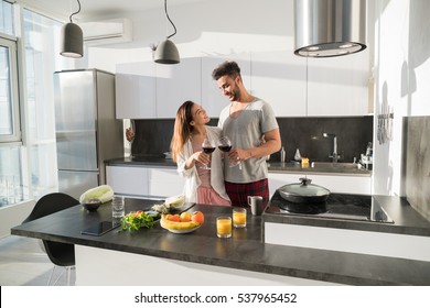 Young Couple Embrace In Kitchen, Hispanic Man And Asian Woman Hug Drink Wine Modern Apartment Interior