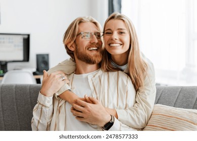 Young couple embraces on their cozy sofa at home, both smiling and radiating love and happiness in their modern living room. Relationship concept - Powered by Shutterstock