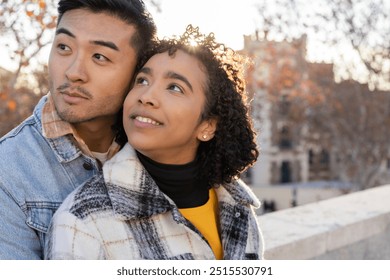 young couple embraces while gazing thoughtfully into the distance during sunset in an outdoor setting. - Powered by Shutterstock