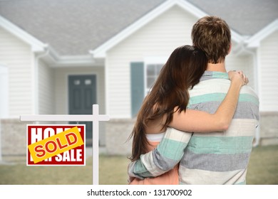 Young Couple Embracing In Front Of House With Sold Sign