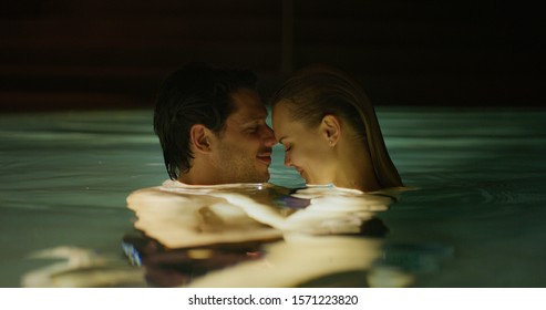  An Young Couple Is Embracing And Having Relax In An Indoor Illuminated With Night Lights Swimming Pool In A Luxury Wellness Center.