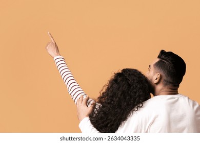 Young couple embracing and pointing up while sitting on floor, rear view