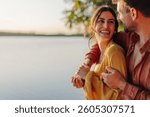 Young couple embracing and smiling by a tranquil lake during sunset, savoring a romantic moment together in the beauty of nature, surrounded by serene evening light