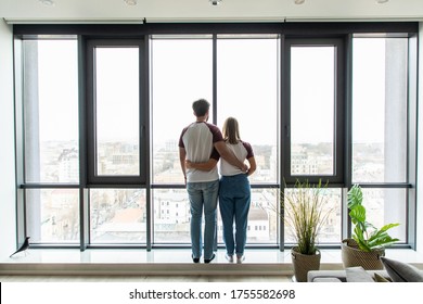 Young couple embracing standing near window and enjoying view from new apartment - Powered by Shutterstock