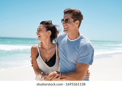 Young couple embracing while walking on beach. Young man and beautiful woman in a relationship enjoing summer vacation in a tropical beach. Happy carefree couple holding hands at seaside feeling free. - Powered by Shutterstock