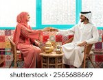 Young couple from Emirati spending time in an arabian traditional cafe. Man and woman wearing kandura and abaya from Dubai conversating together.