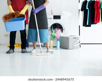 Young couple engages in household cleaning with one holding a bucket and duster while the other mop the floor beside a washing machine or dryer with basket and clothes background - Powered by Shutterstock