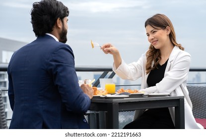 Young couple enjoy breakfast table outdoor on rooftop skyscraper building in cityscape background during sunlight in the morning. Diverse ethnic couple sitting together on roof balcony in skyline view - Powered by Shutterstock