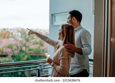 Young couple enjoy drinking wine at balcony. Woman pointing at something.