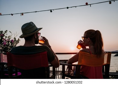 Young couple enjoying beer and sunset in a beach bar - Powered by Shutterstock