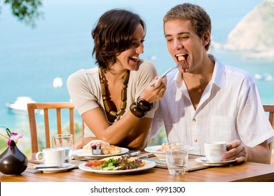 A Young Couple Enjoying Breakfast Outside With An Ocean Backdrop