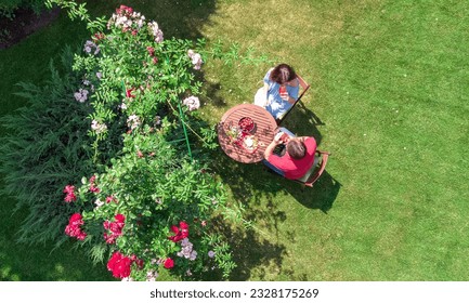 Young couple enjoying food and drinks in beautiful roses garden on romantic date, aerial top view from above of man and woman eating and drinking together outdoors in park - Powered by Shutterstock