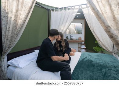 Young couple enjoying a romantic getaway, sitting on a comfortable bed inside a glamping tent, embracing and holding hands, creating a cozy and intimate atmosphere