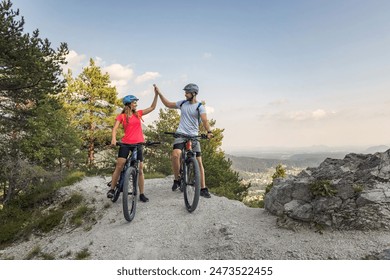 Young couple enjoying spectacular scenery, smiling while sitting on electric mountain bikes and giving a high five to each other. - Powered by Shutterstock