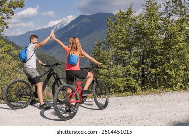 Young couple enjoying spectacular scenery, smiling while sitting on electric mountain bikes and giving a high five to each other. - Powered by Shutterstock