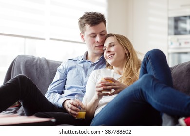 Young couple enjoying themselves on the sofa in the living room. Young man and woman relaxing and drinking the orange juice in the new flat. - Powered by Shutterstock