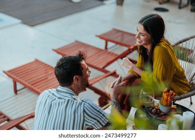 A young couple enjoys a romantic and leisurely conversation over wine, surrounded by a serene poolside setting - Powered by Shutterstock