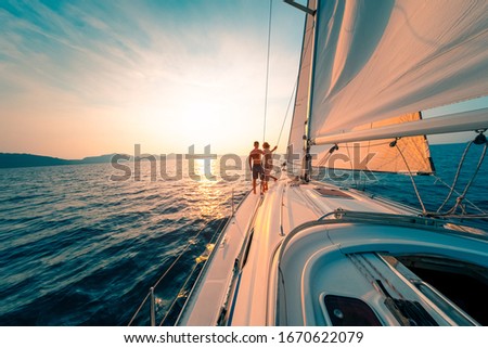 Young couple enjoys sailing in the tropical sea at sunset on their yacht.