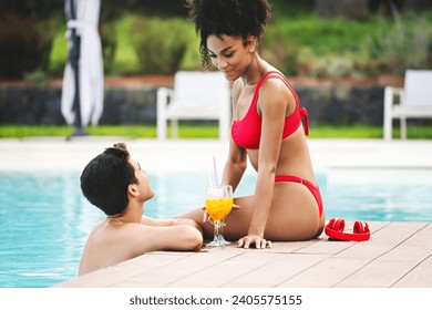 A young couple enjoys a serene poolside moment, sharing a drink and smiles on a sunny vacation. - Powered by Shutterstock