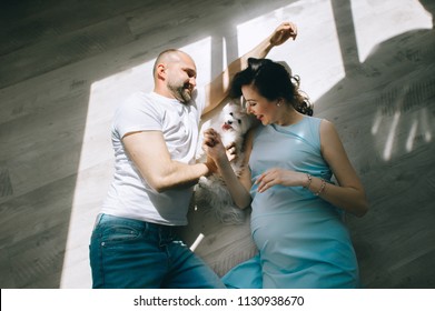 Young Couple Expecting Baby Laying On The Beam Of Light With A Dog Indoors