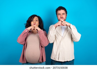 Young Couple Expecting A Baby Standing Against Blue Background Has Rejection Angry Expression Crossing Fingers Doing Negative Sign.