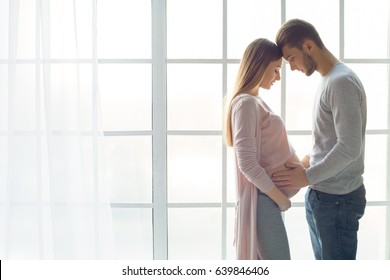 Young couple expecting baby standing together indoors