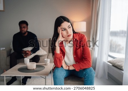 Young couple experiencing relationship problems and emotional distance, sitting separately after an argument in their living room