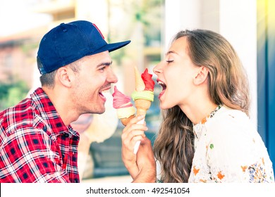 Young Couple Face To Face Eating Ice Cream In Playful Attitude  - Attractive Friends Looking At Each Other Having Fun At Bar Cafe Gelateria - Concept Of Teenagers Romantic Love Moment - Focus On Male