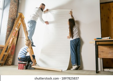 Young Couple, Family Doing Apartment Repair Together Themselves. Mother, Father And Son Doing Home Makeover Or Renovation. Concept Of Relations, Moving, Love. Hanging Wallpaper With Ladder.