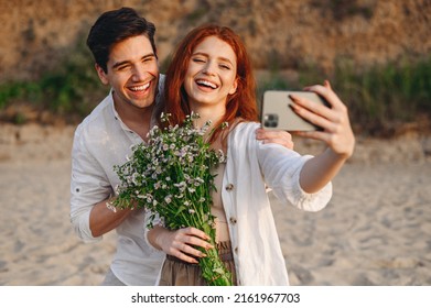 Young couple family man woman wear white clothes hug rest together hold bouquet do selfie shot mobile cell phone post photo social network at sunrise over sea sand beach outdoor seaside in summer day - Powered by Shutterstock