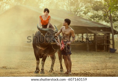 Young couple farmer in village looking together, the woman ride buffalo in the field countryside of Laos on vintage background
