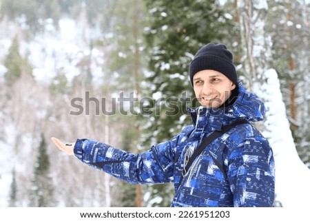 Young couple feeds birds on the winter forest. Small titmouse bird in people's hand. Snow background.