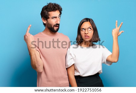 young couple feeling confused and puzzled, showing you are insane, crazy or out of your mind