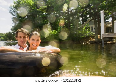 Young Couple Floating In An Inner Tube In A Lake.