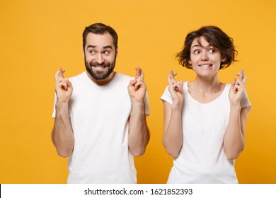 Young couple friends bearded guy girl in white t-shirts isolated on yellow orange background. People lifestyle concept. Mock up copy space. Wait for special moment keeping fingers crossed making wish