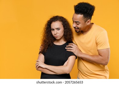 Young couple friends together family african frowning resentful woman man 20s wear black yellow t-shirt hugging offended girlfriend reconciling apologizes isolated on orange background studio portrait