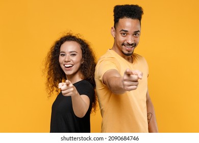 Young couple friends together team family african smiling leader man woman in black t-shirt pointing index finger camera on you motivating encourage isolated on yellow color background studio portrait