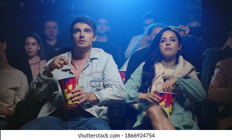 Young Couple Getting Irritated With Man Behind In Movie Theater. Angry Man Looking Back In Cinema. Beautiful Couple Eating Popcorn Indoor. Group Of People Watching Movie In Dark Hall.