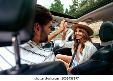 A Young Couple Are Giving Five To Each Other In A New Car. A Man Driving A Car With His Girlfriend And Having Fun. Buying And Renting A Car. Travel, Tourism, Recreation.