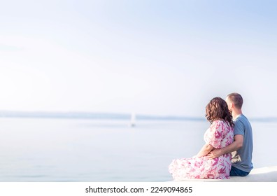 A young couple, a guy and a girl, are sitting on the shore of the lake and looking into the distance. Couple in love, valentine's day. Horizontal photo
