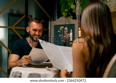 Young couple guy and girl sitting in an Italian restaurant looking at the menu and choosing what to order for dinner while on date