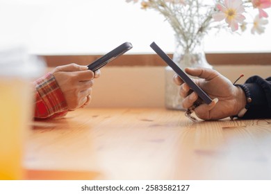 Young couple hands using two phones share social media or talking doing shopping online while sit at table. Mobile tech lifestyle concept