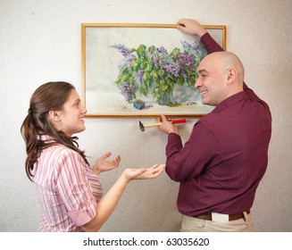 Young Couple Hanging Art Picture On Wall At