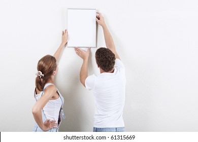 Young Couple Hanging Up Painting On The Wall