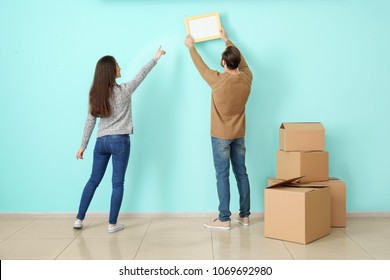 Young Couple Hanging Picture On Wall In Their New House