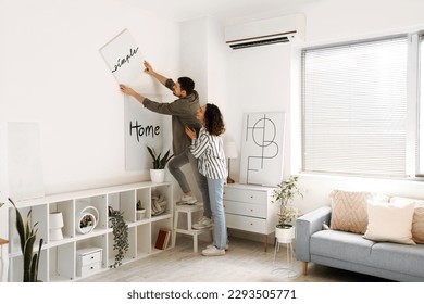 Young couple hanging poster on light wall at home - Powered by Shutterstock