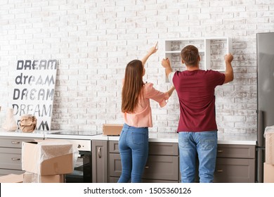 Young Couple Hanging Shelf On Wall In Their New House