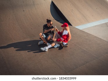 Young Couple Hangout In Skate Park While Sitting On Skateboard.