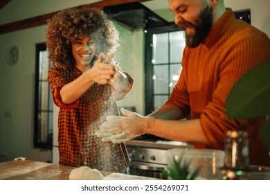 Young couple happily making dough in a modern kitchen, covered in flour and clapping hands, enjoying a fun cooking activity filled with love and laughter - Powered by Shutterstock